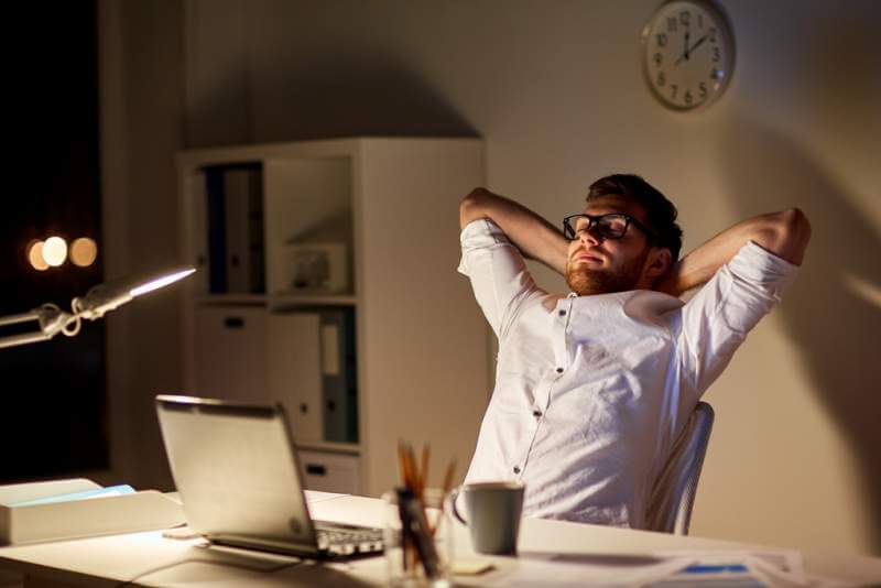 man-with-laptop-stretching-at-night-office