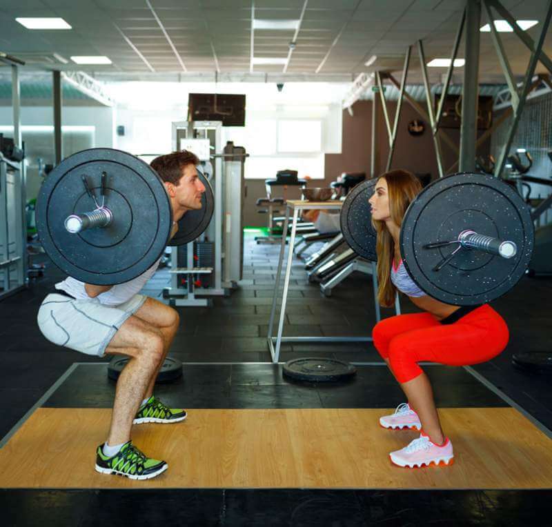 athletic-man-and-woman-with-barbell-doing-squats