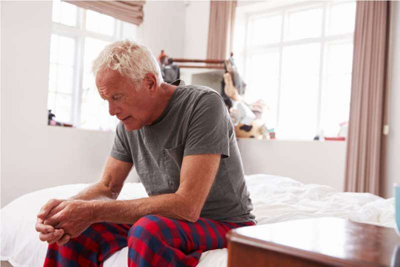 homme âgé assis sur son lit à la maison souffrance