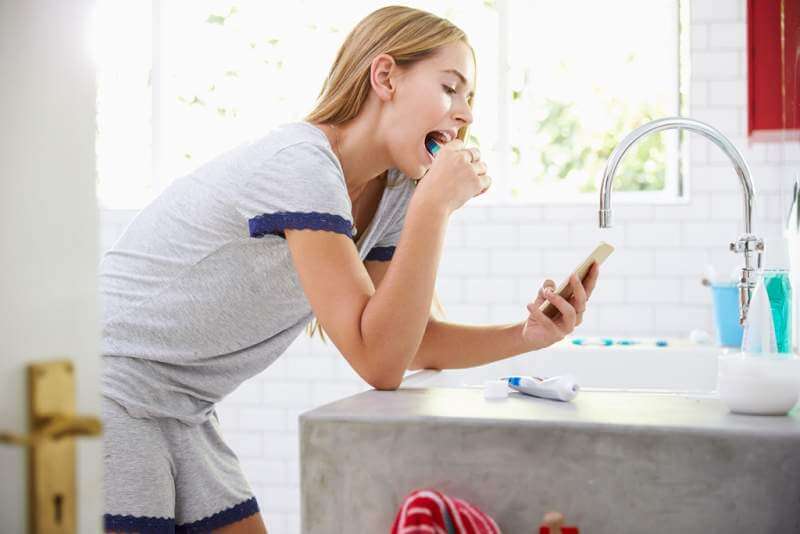 woman-in-pajamas-brushing-teeth-and-using-mobile