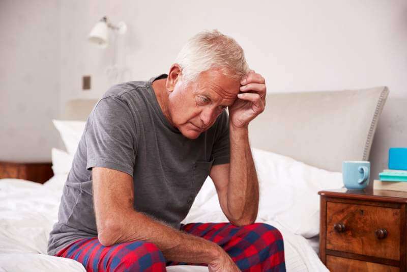 senior-man-sitting-on-bed-at-home-suffering