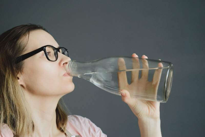 woman-in-glasses-drinks-water-from-glass-bottle