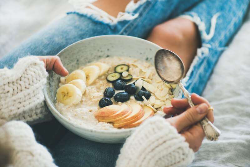 woman-in-jeans-and-sweater-eating-healthy-oatmeal