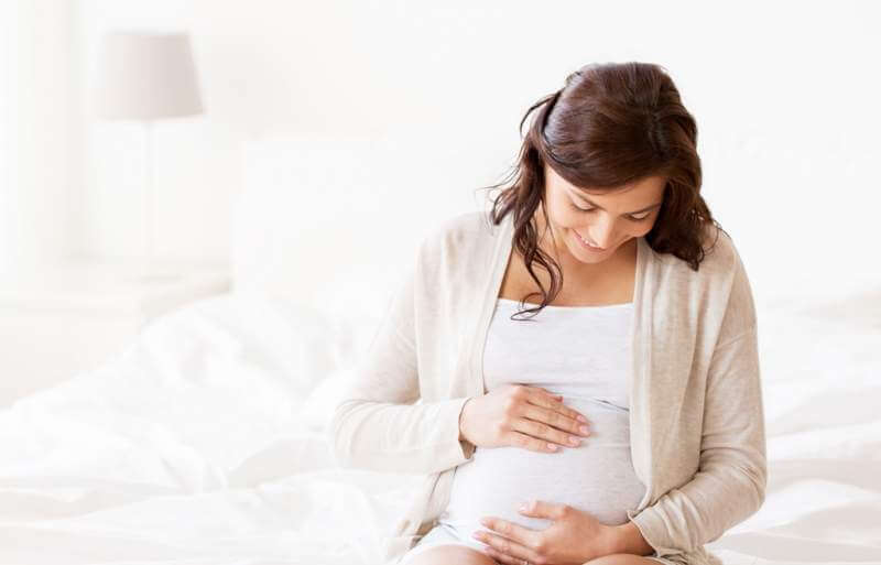 happy-pregnant-woman-sitting-on-bed-at-home