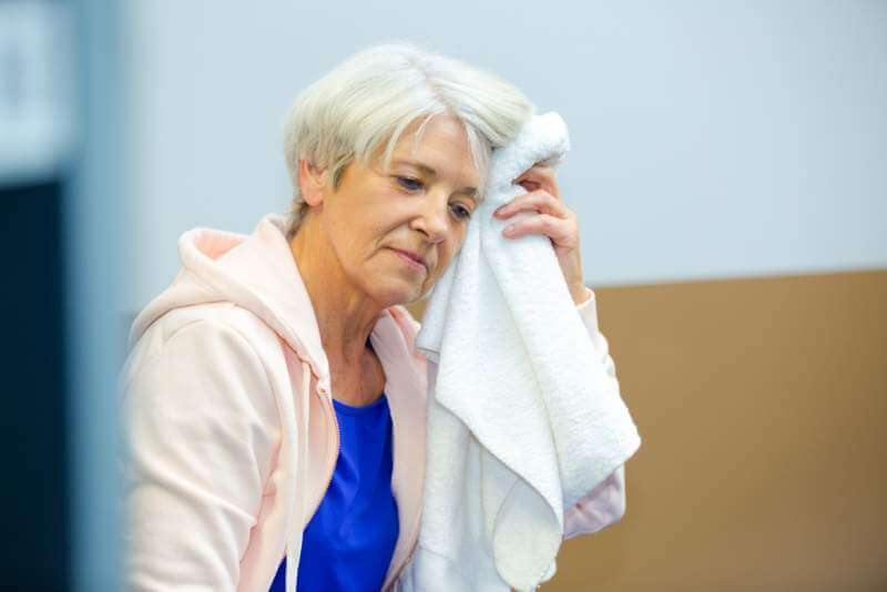 senior-woman-mopping-brow-with-towel-after