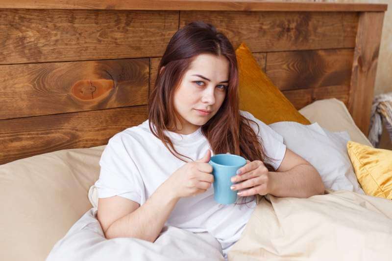half-asleep-young-woman-drinking-coffee-on-bed